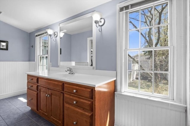 bathroom with vanity, wainscoting, tile patterned flooring, and vaulted ceiling