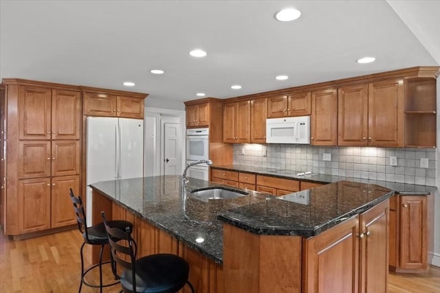 kitchen featuring a sink, brown cabinets, white appliances, and light wood-style flooring