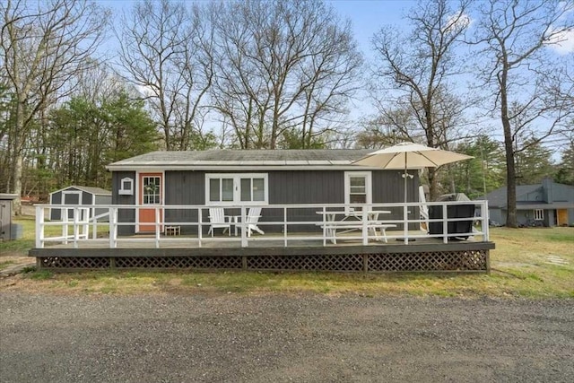 rear view of property featuring a deck, a storage unit, and an outbuilding