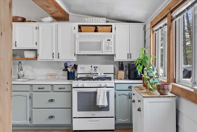 kitchen with white appliances, a sink, vaulted ceiling, light countertops, and white cabinets