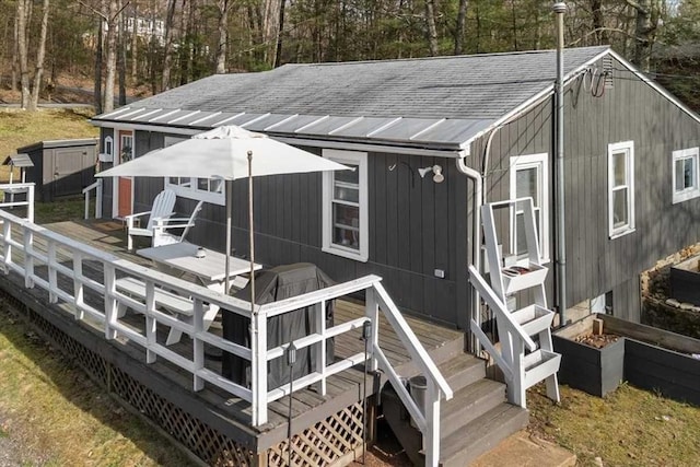 back of house featuring a deck, a shingled roof, a storage shed, and an outbuilding