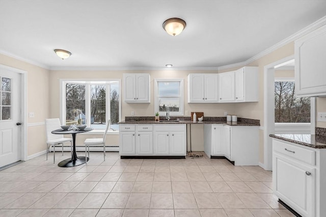 kitchen with light tile patterned floors, a sink, white cabinetry, ornamental molding, and dark stone countertops