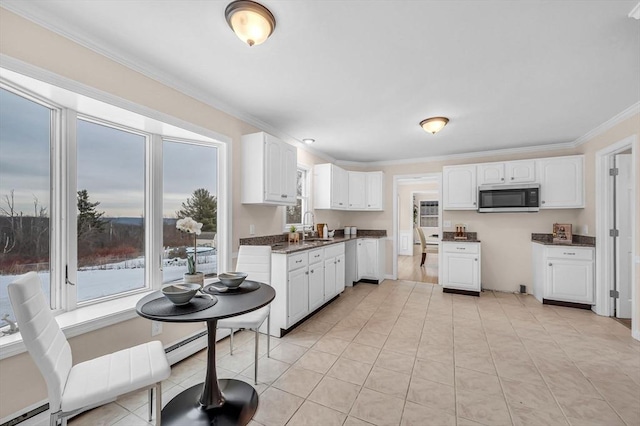 kitchen with a sink, white cabinetry, ornamental molding, stainless steel microwave, and dark countertops