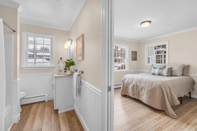 bedroom featuring a wainscoted wall, light wood-style flooring, baseboard heating, and crown molding