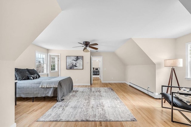 bedroom with light wood-style floors, a baseboard heating unit, a ceiling fan, vaulted ceiling, and baseboards