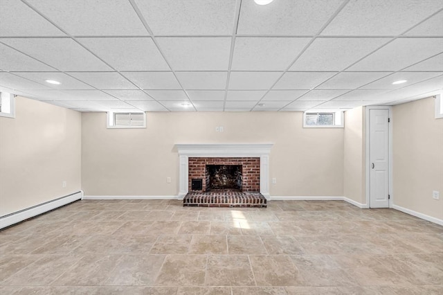 basement with a brick fireplace, baseboards, baseboard heating, and a wealth of natural light