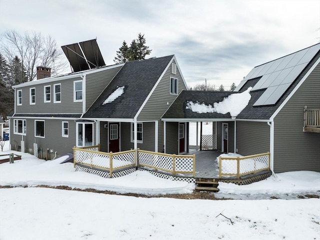 snow covered back of property with solar panels, a shingled roof, and a chimney