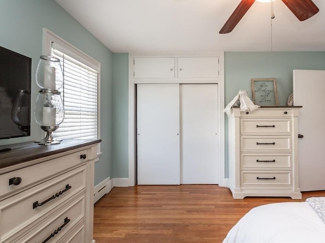 bedroom featuring baseboard heating, ceiling fan, a closet, and light wood-type flooring