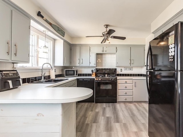 kitchen with sink, gray cabinetry, black appliances, kitchen peninsula, and backsplash