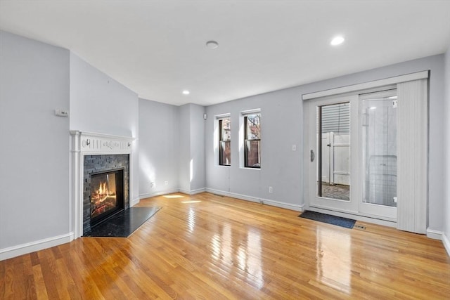 unfurnished living room featuring baseboards, recessed lighting, a glass covered fireplace, and wood finished floors