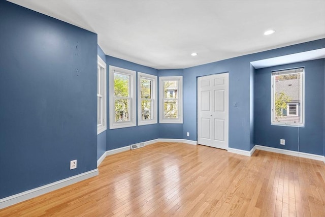 unfurnished bedroom with multiple windows, hardwood / wood-style flooring, and visible vents