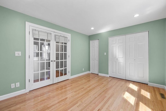 unfurnished bedroom featuring two closets, baseboards, french doors, and wood finished floors