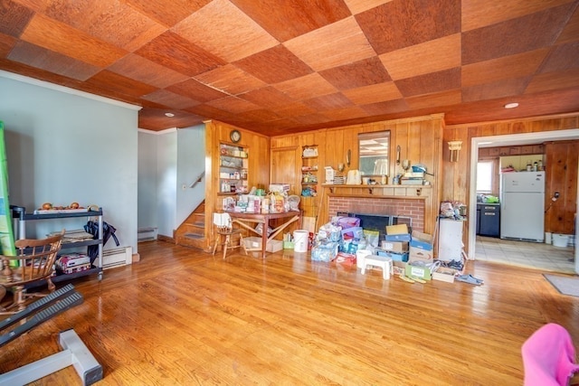 interior space with light tile flooring, wooden walls, a brick fireplace, a baseboard heating unit, and crown molding