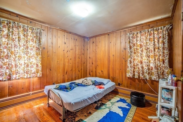 bedroom with wood walls, a baseboard radiator, and light hardwood / wood-style flooring