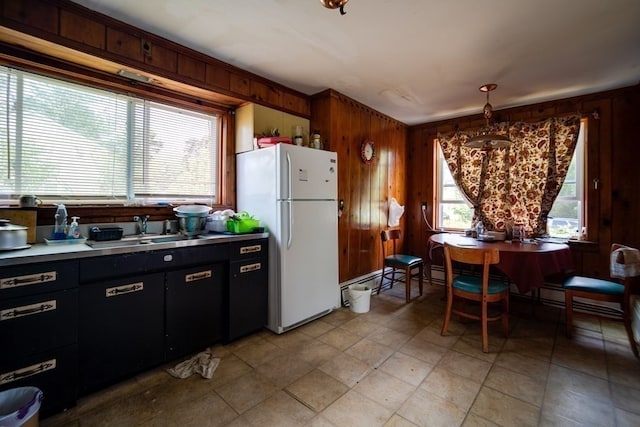 kitchen featuring light tile floors, white fridge, wooden walls, hanging light fixtures, and sink