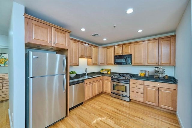 kitchen featuring visible vents, dark countertops, light wood-type flooring, a sink, and appliances with stainless steel finishes