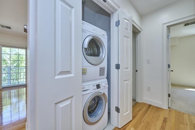 laundry area featuring laundry area, stacked washing maching and dryer, visible vents, and light wood-style floors