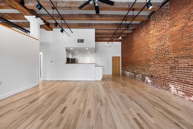 33 Sleeper St Unit 104, Boston, MA 02210 - unfurnished living room featuring a high ceiling, a ceiling fan, brick wall, wood finished floors, and beam ceiling