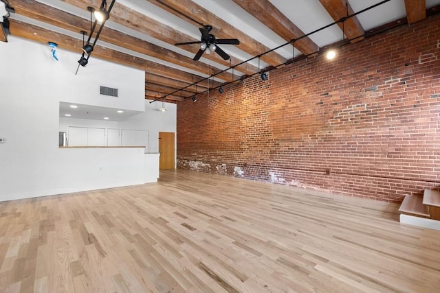 33 Sleeper St Unit 104, Boston, MA 02210 - unfurnished living room featuring brick wall, a high ceiling, beamed ceiling, wood finished floors, and ceiling fan