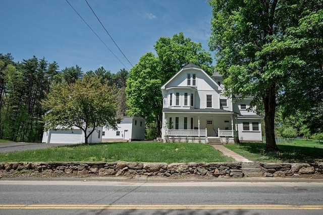 victorian-style house featuring a porch, a front yard, a garage, and driveway