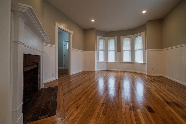 unfurnished living room featuring wood finished floors, a brick fireplace, wainscoting, and recessed lighting