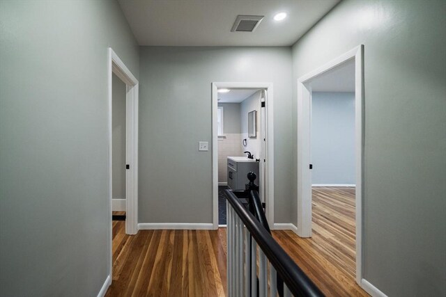 hall with dark wood finished floors, baseboards, a sink, recessed lighting, and an upstairs landing