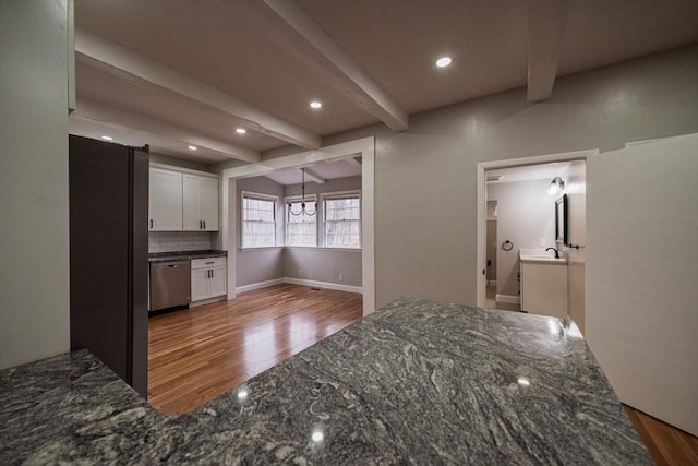 kitchen with dishwasher, wood finished floors, white cabinetry, dark stone counters, and beamed ceiling