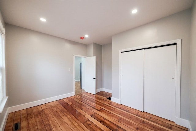unfurnished bedroom featuring hardwood / wood-style floors, a closet, baseboards, and recessed lighting
