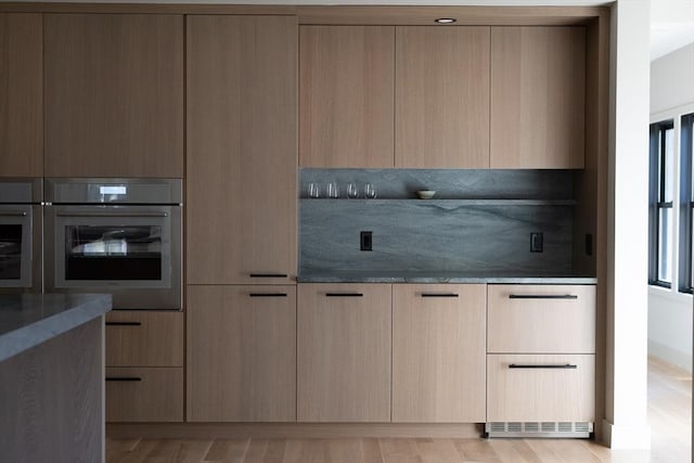 kitchen featuring light brown cabinetry, light hardwood / wood-style floors, oven, and stone counters