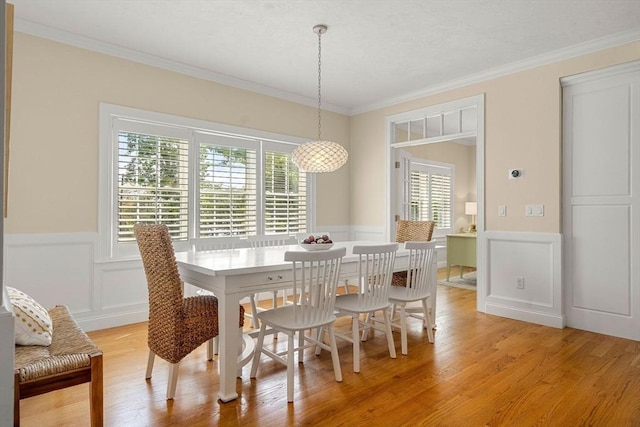 dining space featuring a wainscoted wall, light wood-style flooring, crown molding, and a decorative wall