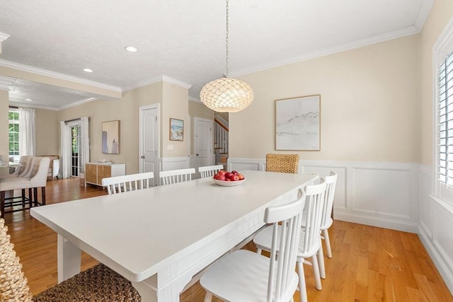 dining space featuring stairway, light wood-style flooring, crown molding, and a wainscoted wall