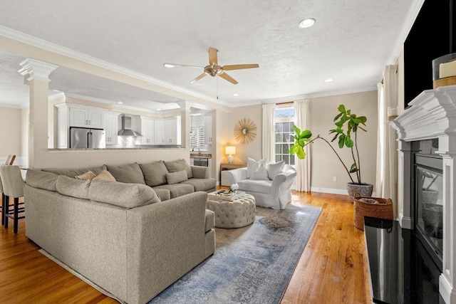 living area with crown molding, baseboards, decorative columns, light wood-style flooring, and a glass covered fireplace