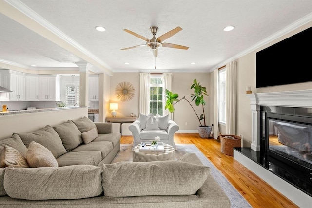 living area featuring a glass covered fireplace, recessed lighting, light wood-style floors, crown molding, and baseboards