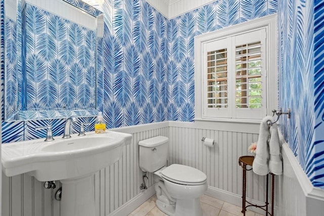 bathroom with wallpapered walls, baseboards, toilet, wainscoting, and tile patterned floors