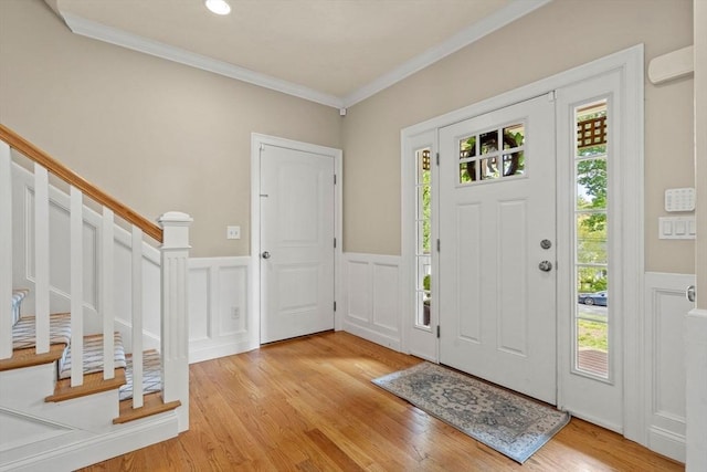 foyer with stairs, ornamental molding, light wood-style floors, and wainscoting