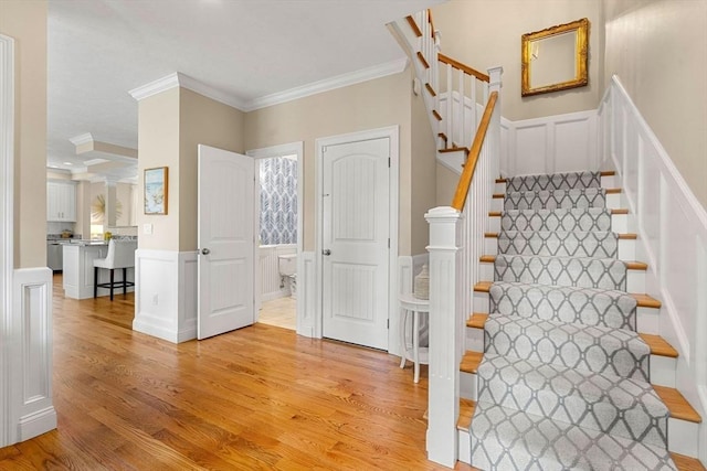 stairway with wood finished floors, ornamental molding, and a decorative wall