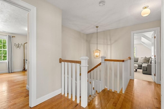 hall featuring baseboards, an upstairs landing, a textured ceiling, and light wood finished floors