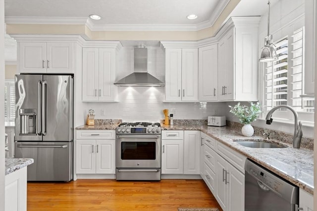 kitchen with light wood-style flooring, appliances with stainless steel finishes, white cabinetry, wall chimney exhaust hood, and a sink