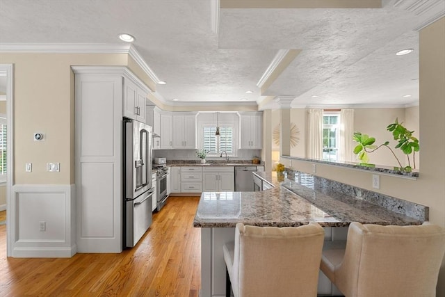 kitchen featuring light wood finished floors, a breakfast bar area, ornamental molding, appliances with stainless steel finishes, and a textured ceiling