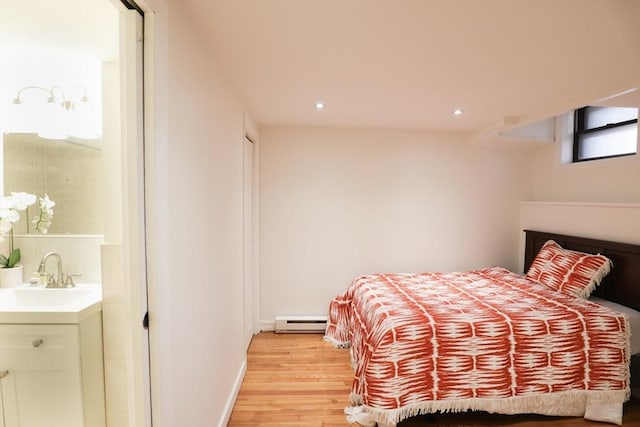 bedroom with light wood-type flooring, a baseboard radiator, and sink