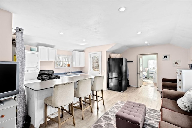 kitchen with a breakfast bar area, lofted ceiling, light wood-style floors, a peninsula, and black appliances