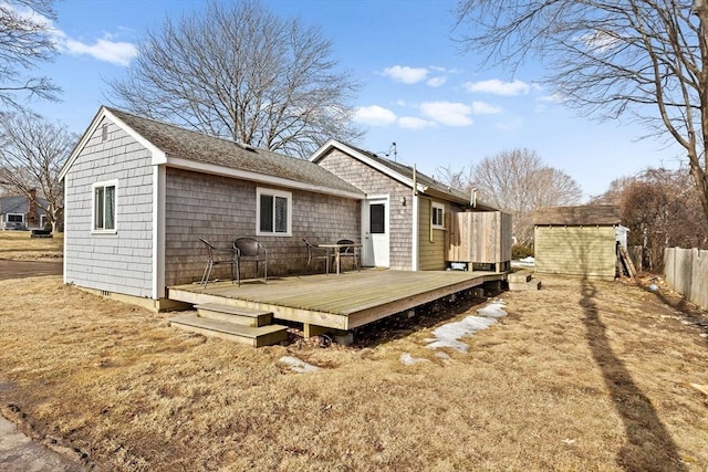 back of property with an outbuilding, roof with shingles, fence, a shed, and a wooden deck