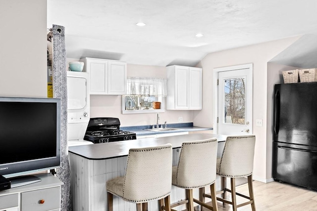 kitchen with light wood-style flooring, a breakfast bar area, black appliances, white cabinetry, and a sink