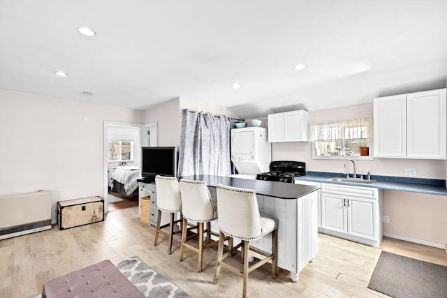 kitchen featuring a breakfast bar, light wood-style flooring, white cabinets, a kitchen island, and a sink