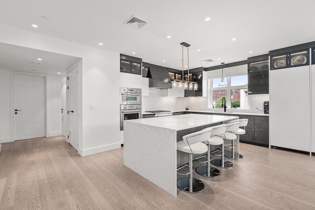 69 Walnut St Unit 4, Brookline, MA 02445 - kitchen with dark cabinetry, double oven, a center island, wall chimney exhaust hood, and recessed lighting