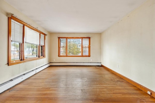 unfurnished room with a baseboard heating unit, a wealth of natural light, baseboards, and light wood finished floors