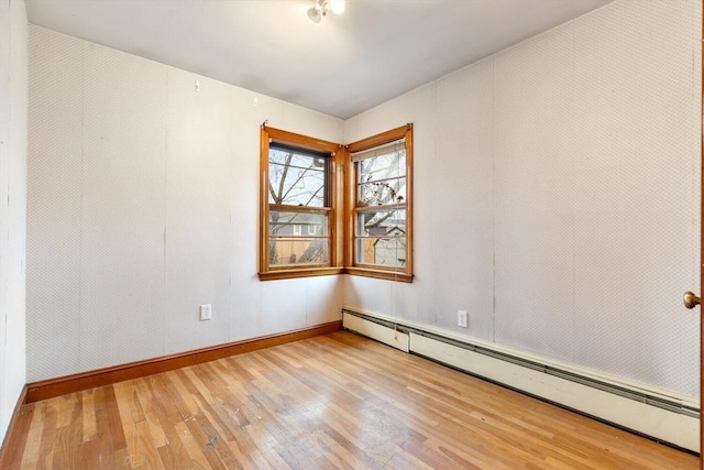 empty room featuring baseboard heating, wood finished floors, and baseboards