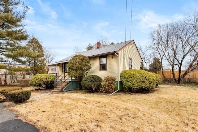 view of front of home with a shingled roof, a chimney, and a front yard