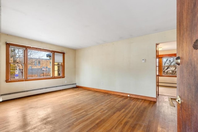 spare room featuring a healthy amount of sunlight, baseboard heating, and wood finished floors