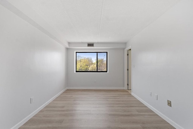unfurnished room with baseboards, light wood-style flooring, a textured ceiling, and visible vents